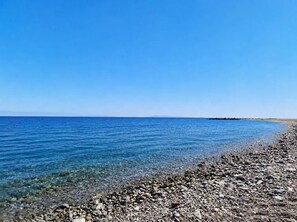 Ein Kiesstrand mit klarem, blauem Wasser und einer entfernten Landmasse.