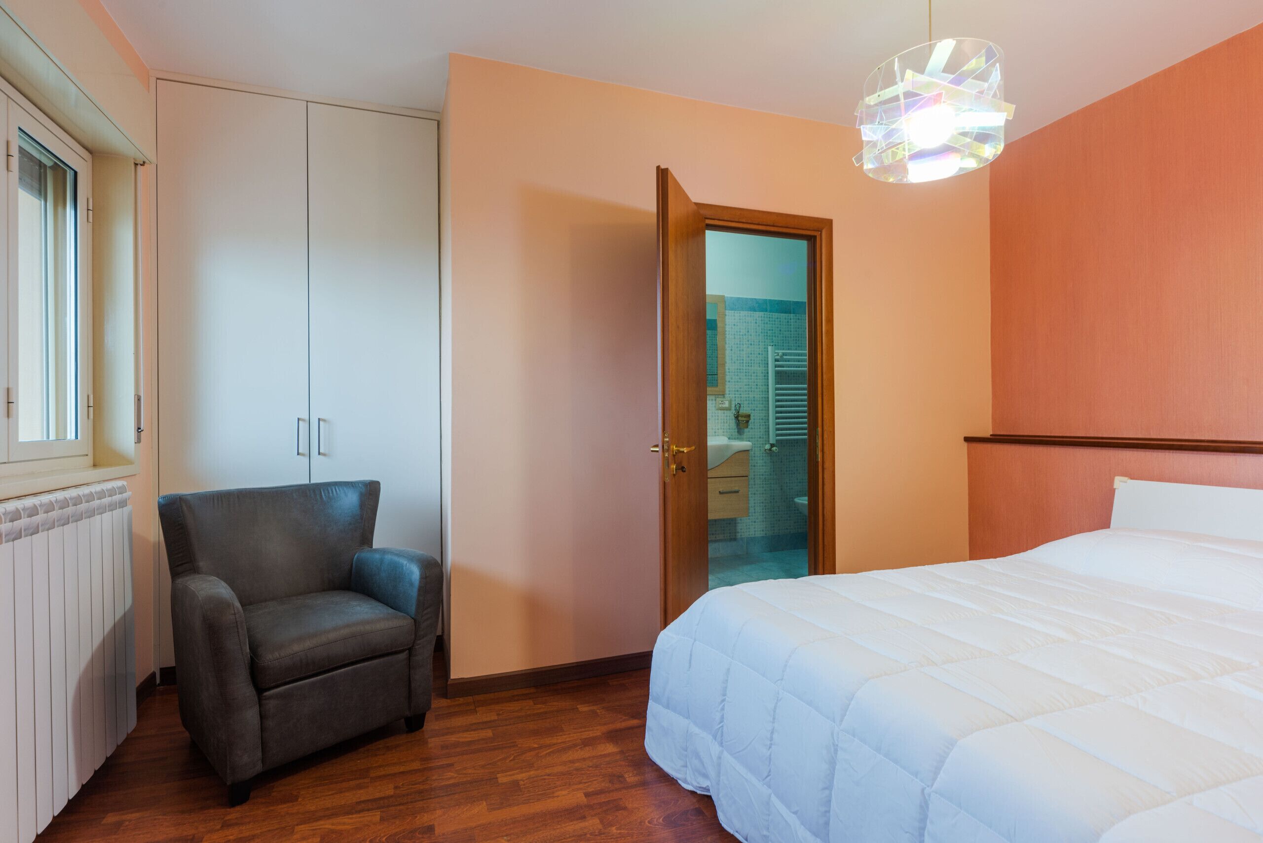Un dormitorio con cama, una silla, un armario y una puerta que da a un baño.