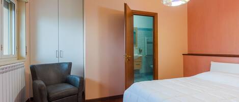 Un dormitorio con cama, una silla, un armario y una puerta que da a un baño.