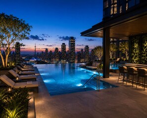 A rooftop infinity pool with lounge chairs, a bar area, and a city skyline view at dusk. - Greenfield residence by sunway pyramid (Petaling Jaya)
