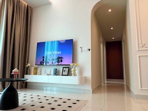 Una sala de estar moderna con un televisor de pantalla plana en una pared blanca, una mesa de centro negra y un tapete estampado.