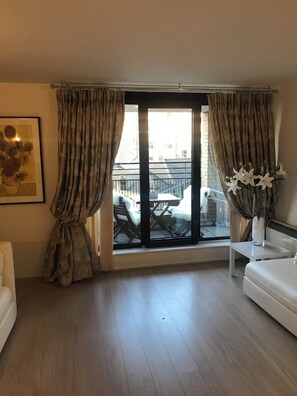 Een kamer met een grote schuifpui, een witte bank, een tafeltje en een kunstwerk in een lijst aan de muur.