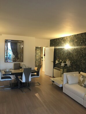 Een moderne woonkamer met een eethoek, een witte bank, een salontafel en een grote spiegel.