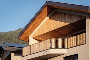 Un edificio moderno con fachada de madera, un balcón con listones verticales y paneles solares en el techo.