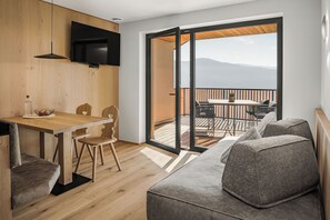 Una habitación moderna con una mesa de comedor de madera, un sofá y un balcón con vistas a las montañas.