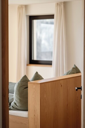 A bedroom with a wooden wardrobe, a window with curtains, and a bed with pillows. - Oachner Living | Design vacation apartments with sauna in South Tyrol (Trentino-Alto Adige)
