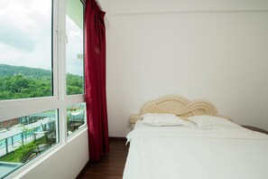 A hotel room with a bed, a window with a red curtain, and a view of greenery outside. - Trival Celes Homestay @ Sri Indah Sandakan (Sandakan)