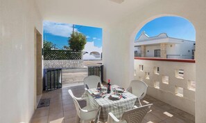 A patio with a table set for dining, white chairs, and a view of a white building and tree.