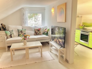 A cozy living room with a sofa, a flat-screen TV, a coffee table, and a kitchen area with green cabinets. - "GOLDREGEN" A place of the soul for silence, forest bathing & a studio for artists' souls (Forbach Hundsbach)