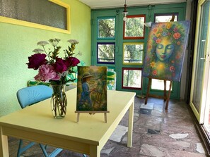 A room with a table, a vase of flowers, an easel with a painting, and a window with a view of trees. - "GOLDREGEN" A place of the soul for silence, forest bathing & a studio for artists' souls (Forbach Hundsbach)