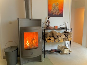 A wood-burning stove with a fire, a stack of firewood, and a decorative sculpture on a shelf. - "GOLDREGEN" A place of the soul for silence, forest bathing & a studio for artists' souls (Forbach Hundsbach)