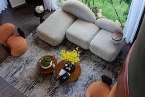 A modern living room with a sectional sofa, round ottomans, a coffee table with a vase of yellow flowers, and a small side table with a plant. - House of Gaia (Lipa City)