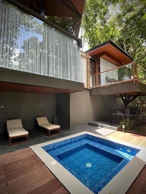 Uma área moderna com piscina ao ar livre, piscina retangular, duas espreguiçadeiras e um deck de madeira.