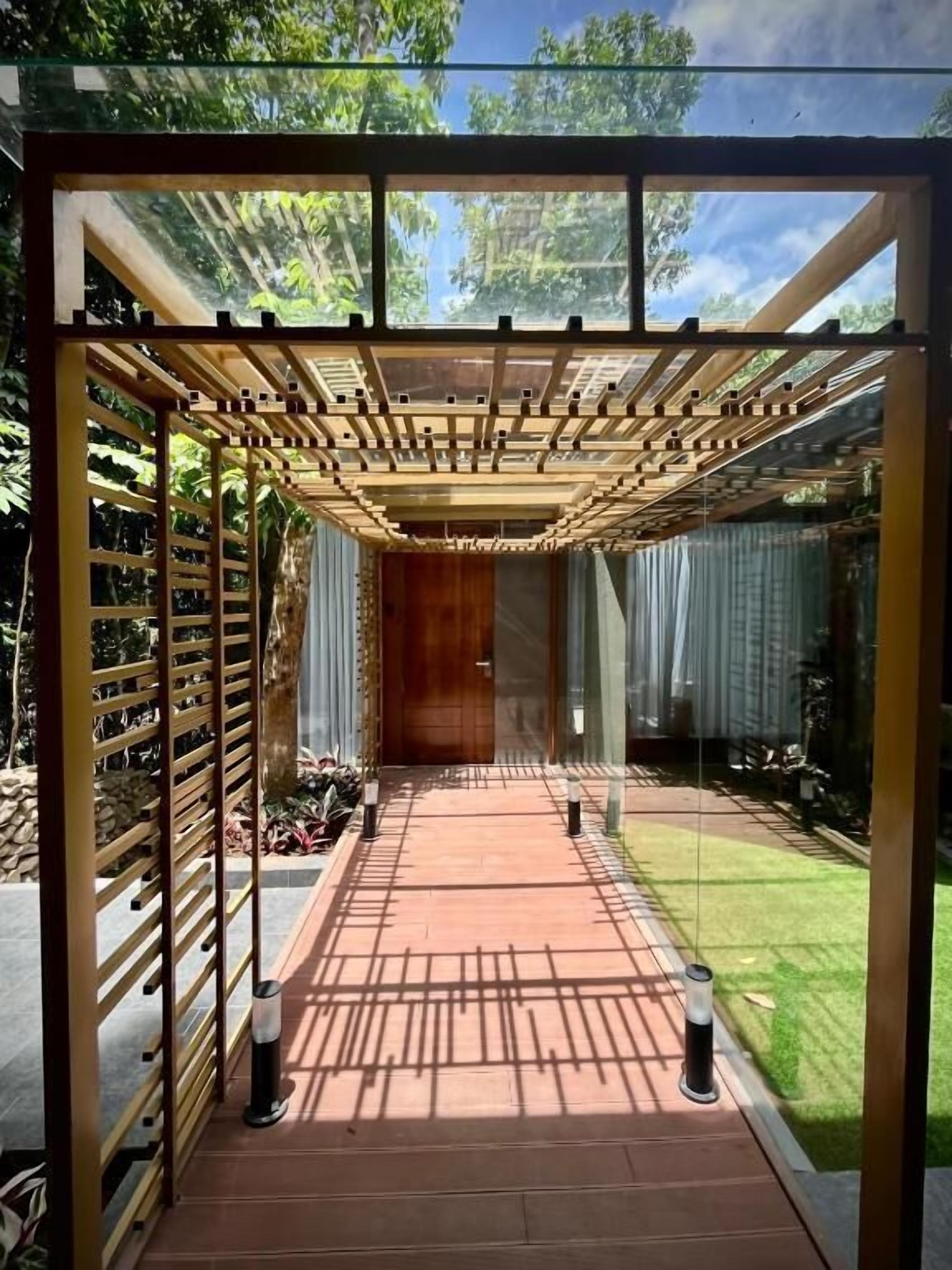 A covered outdoor area with a wooden pergola, a pathway, and a glass enclosure.