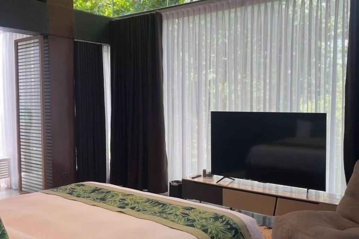 A hotel room with a bed, a TV, and a window with curtains.