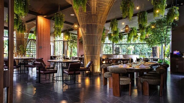 A restaurant with high ceilings, hanging plants, and a mix of seating arrangements including tables and chairs.