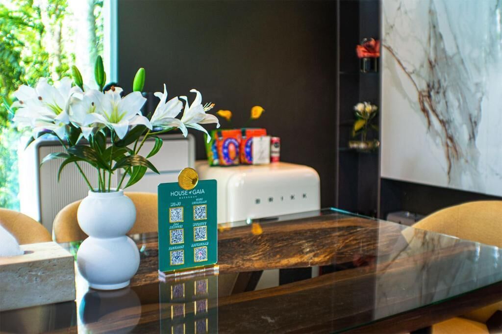 A hotel reception area with a glass table, white flowers, a QR code sign, and a marble wall.