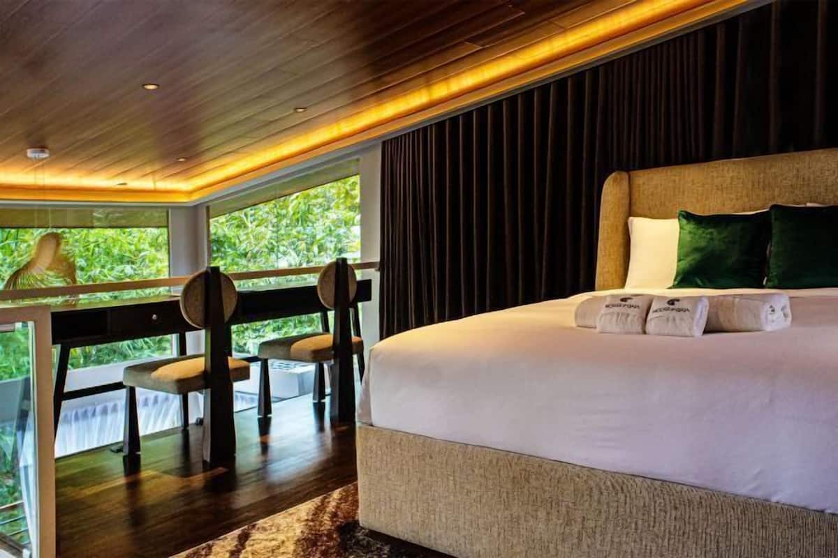 Un dormitorio con una cama grande, escritorio y sillas, vistas a zonas verdes y techo de madera.