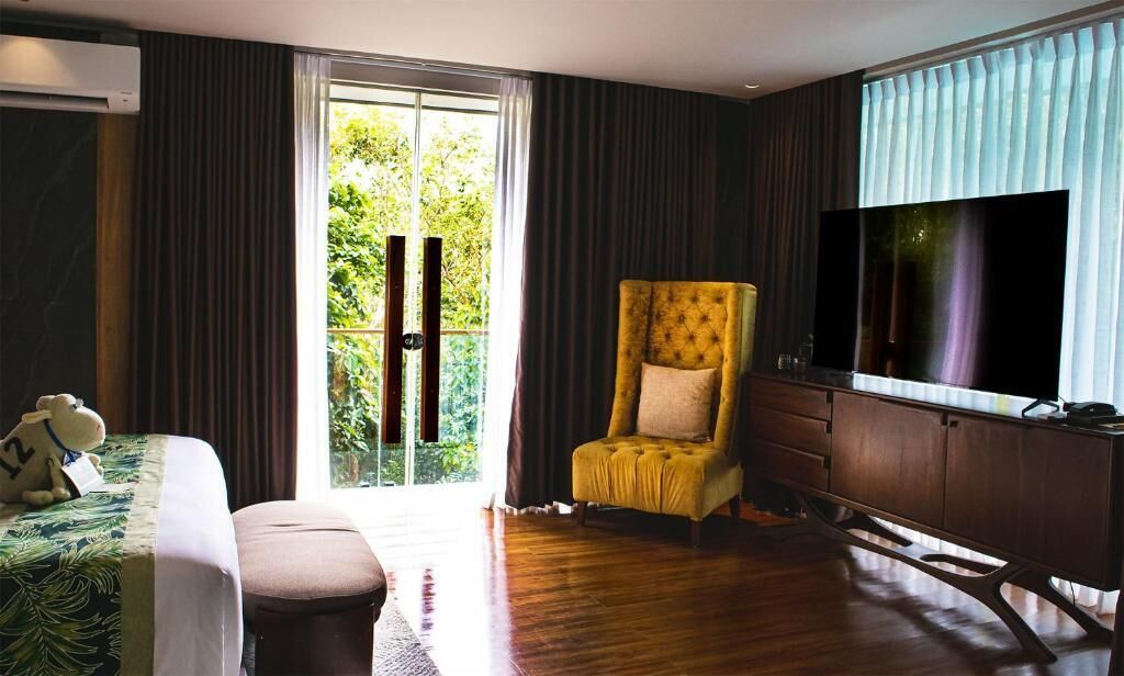 A hotel room with a bed, a chair, a desk, a TV, and a sliding glass door to a balcony.