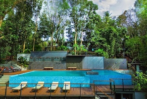Piscina com espreguiçadeiras, rodeada por vegetação densa e um muro de pedra.