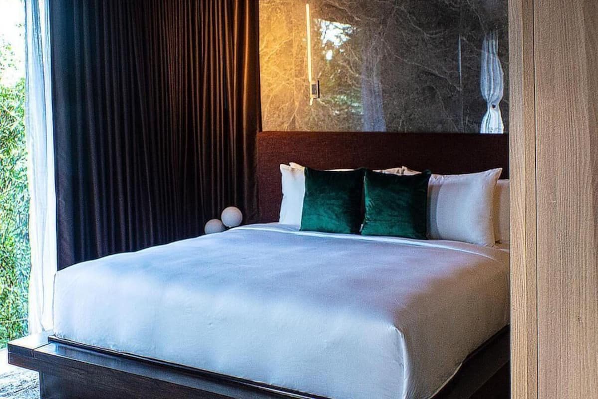 Un dormitorio moderno con una cama grande, cortinas oscuras y vistas a árboles por la ventana.