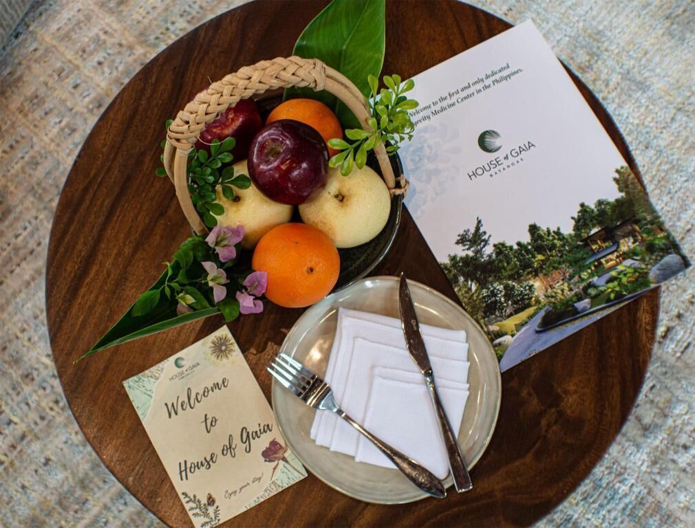 Une carte de bienvenue, un panier de fruits et une brochure sur une table en bois.