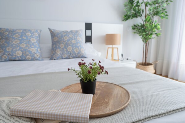 A neatly arranged bedroom with a bed, pillows, a bedside table, a lamp, and a potted plant.