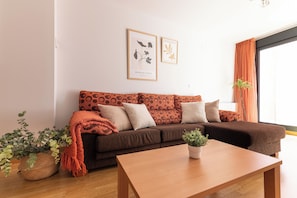 A living room with a brown sofa, two framed botanical prints, a wooden coffee table, and a potted plant.