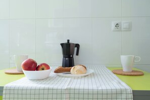 A kitchen counter with a coffee maker, a bowl of fruit, and a plate with bread.