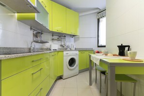A kitchen with green cabinets, a washing machine, a coffee maker, and a table with a cup and a plate.
