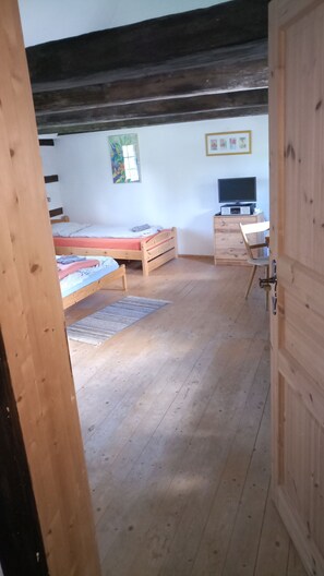 A bedroom with a wooden bed, a desk with a chair, a television, and a window with artwork.