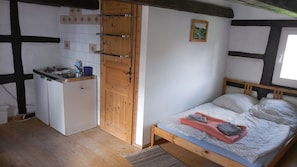 Ein kleiner, kompakter Raum mit einer Küchenzeile, einem Bett mit gemustertem Überwurf und einem kleinen Gemälde an der Wand.