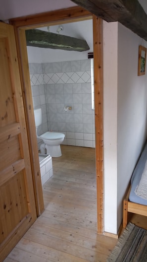 Eine Holztür führt in ein Badezimmer mit Toilette, gefliesten Wänden und Holzboden.