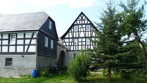 Ett traditionellt hus med korsvirkesfasad och ett sluttande tak, en liten trädgård med ett träd och en blå tunna.