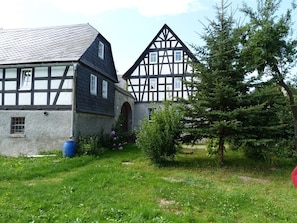 Ein traditionelles Fachwerkhäuschen mit geneigtem Dach, einem kleinen Garten mit Baum und einem blauen Fass.