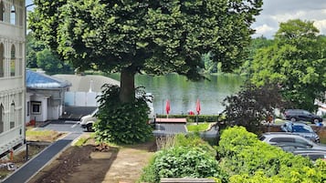 Ein von Bäumen gesäumter Innenhof mit Seeblick, ein Parkplatz mit Autos und ein Gebäude mit blauem Dach.