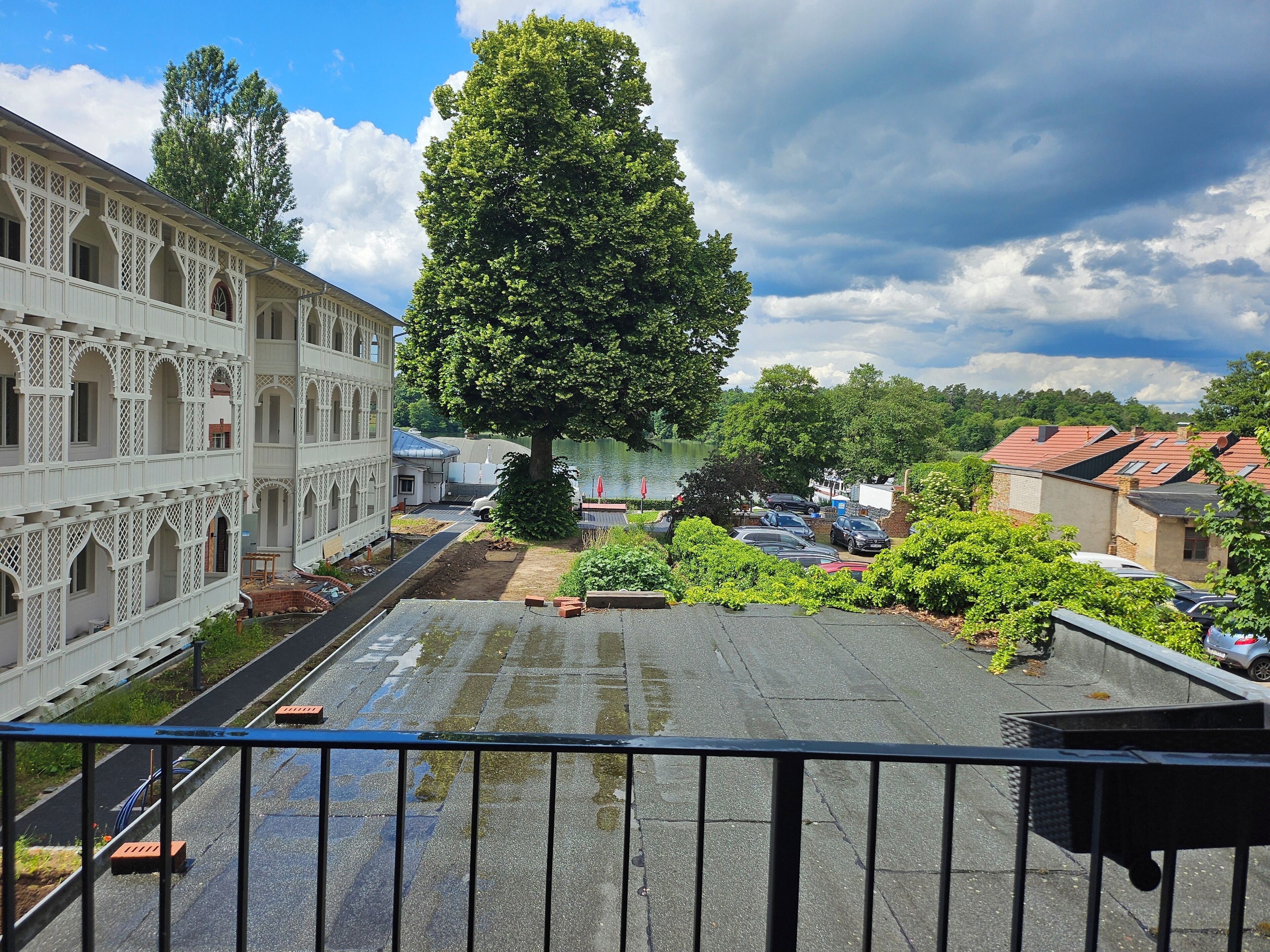 Ein Innenhof mit einem großen Baum, einem Gebäude mit Rundbogenfenstern und einem Parkplatz.