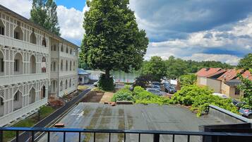 Ein Innenhof mit einem großen Baum, einem Gebäude mit Rundbogenfenstern und einem Parkplatz.