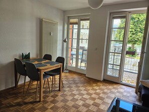 A dining area with a checkered wooden floor, a table with chairs, a radiator, and a view through glass doors to an outdoor area with a table and chairs. - Centrally located vacation apartment with a balcony overlooking the lake. 250 m from Rheinsberg Castle (Rheinsberg)