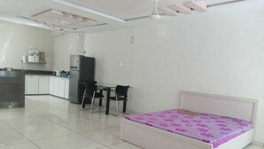 A modern bedroom with a bed, a desk, and a kitchenette. - Hotel nova galaxy  (Rajkot)