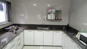 A kitchen with white cabinets, a countertop, a sink, and a window. - Hotel nova galaxy  (Rajkot)
