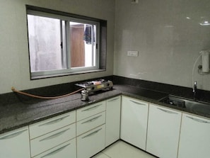 Une petite cuisine avec des meubles blancs, un plan de travail noir, une fenêtre et une cuisinière à gaz.
