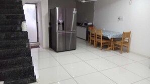 A kitchen with a refrigerator, wooden chairs, and a dining table. - Hotel nova galaxy  (Rajkot)