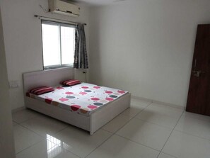 Une chambre à coucher avec un lit, une fenêtre avec des rideaux, une porte et un climatiseur fixé au mur.