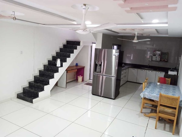 A modern kitchen with a stainless steel refrigerator, a dining table with chairs, and a staircase with a black railing. - Hotel nova galaxy (Rajkot)