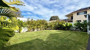 A well-maintained backyard with a lawn, various tropical plants, and a two-story building with balconies.