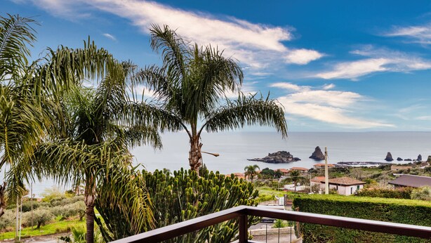 Un balcon offrant une vue sur la mer, les palmiers et les formations rocheuses lointaines.