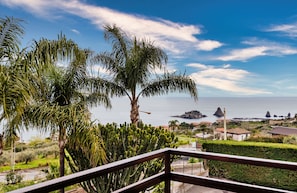 A balcony with a view of the sea, palm trees, and distant rocky formations. - Faraglioni Sea View Terrace by Wonderful Italy (Aci Catena)