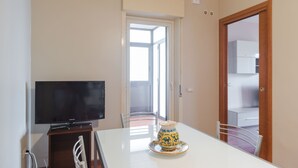 Un coin repas équipé d’un téléviseur, d’une table agrémentée d’un vase décoratif, de chaises et d’une porte donnant sur un balcon.