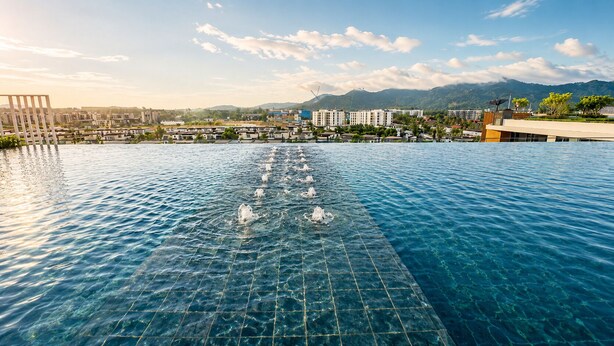 Ein Schwimmbecken mit klarem Wasser, umgeben von Gebäuden und Bergen im Hintergrund.